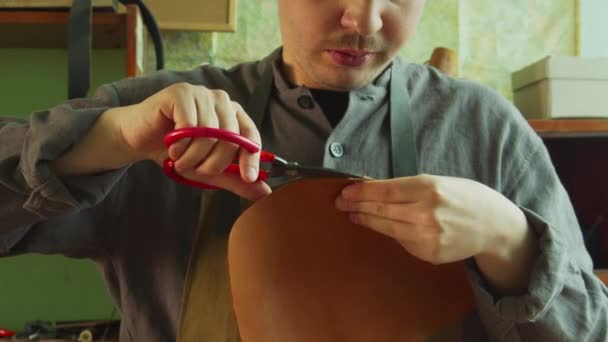 Preparación para la creación de zapatos de cuero genuino. El zapatero corta el borde de una pieza de cuero con tijeras de sastres. — Vídeos de Stock