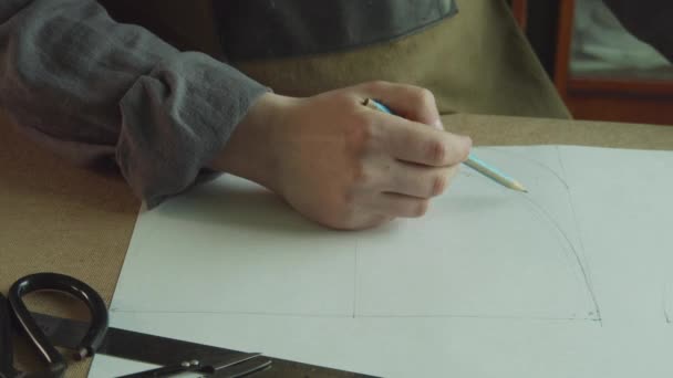 Το χέρι ράφτες με ένα μολύβι σχεδιάζει το σχήμα των προτύπων για τους συγγραφείς παπούτσια σε χαρτί. — Αρχείο Βίντεο