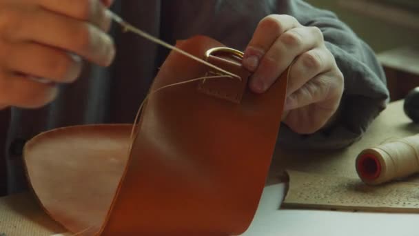 Primer plano del proceso de coser la sujeción del asa de una bolsa de cuero. Las manos del sastre ponen el hilo en los agujeros. — Vídeos de Stock