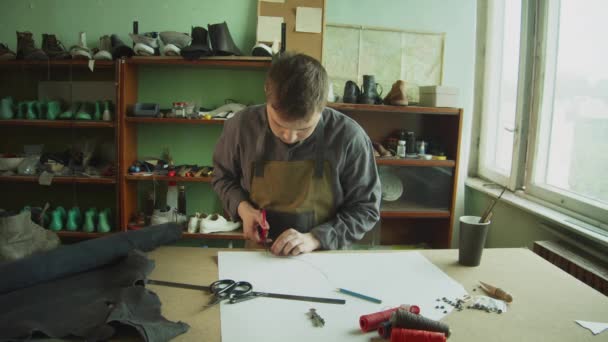 ワークショップの靴職人は手作りの革製品を生産しています。はさみで靴の形を切り取る. — ストック動画