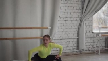 Genç bir kız, dans salonunda, tuğla duvara ve pencereye karşı modern bir dans eder.