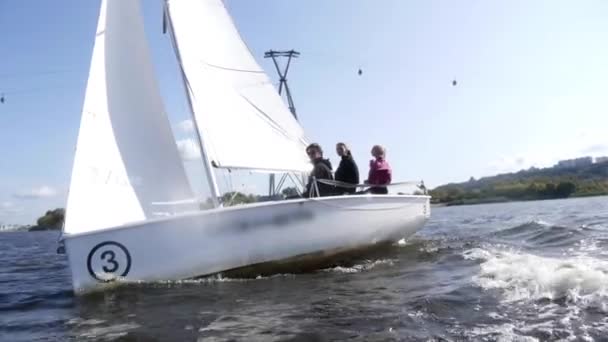 Egy fehér jachton fehér vitorlával három fiatal lebeg a folyón a felvonó alatt lassított felvételen.. — Stock videók