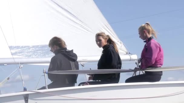 En självsäker kille i solglasögon och två vackra flickor poserar på en yacht mot den blå himlen på en solig dag i slowmotion — Stockvideo