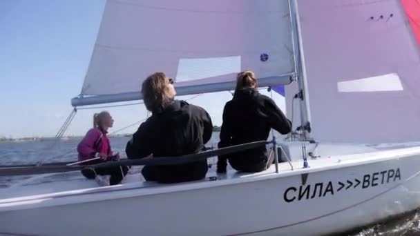 Trois amis un mec et une fille profitent du soleil et d'une promenade sur la rivière sur un voilier sous une grande voile multicolore — Video