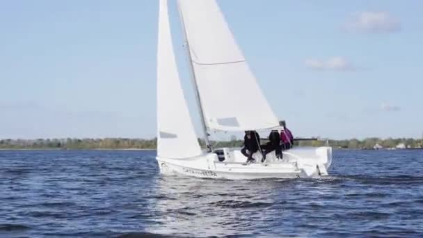 Egy fehér vitorlás jacht három barátjával a fedélzeten úszik a tó felszínén.. — Stock videók