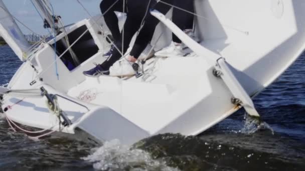 Slow motion schot. Aan boord van een wit zeiljacht zitten twee meisjes en een man, ze controleren het zeil met hun handen en voeten — Stockvideo