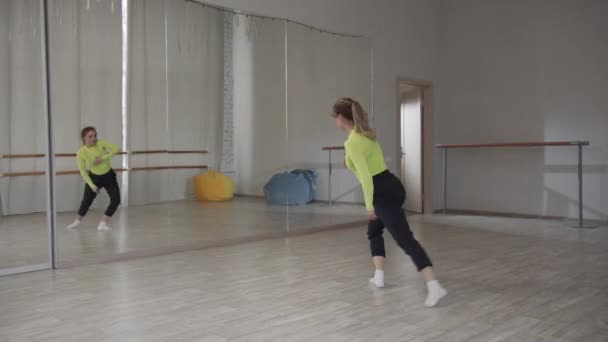 Uma menina bonita dança na frente de um espelho e preens durante um treino de dança no ginásio — Vídeo de Stock