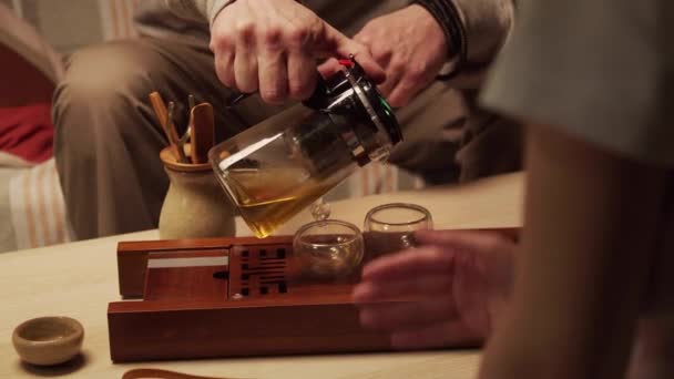 De cerca. Un maestro de ceremonia del té asiático enseña a un estudiante el misterio de preparar té de hierbas chino en una tetera. — Vídeos de Stock