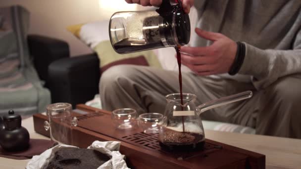 Neznámý muž nalévá uvařený čaj z konvice do džbánu, z džbánu do skleněné mísy a popíjí, zatímco sedí na pohovce — Stock video