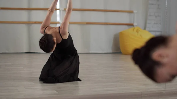 На репетиции в балетной школе красивая танцовщица растягивает шею и спину перед зеркалом — стоковое фото