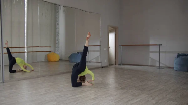 Een set van mooie bewegingen in de hedendaagse dans. Een meisje in een geel t-shirt en een zwarte stretch broek danst op de studio vloer. Springen met splits. — Stockfoto