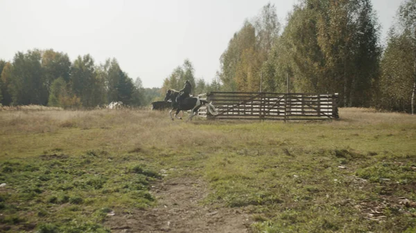 Doświadczony jeździec pokazuje kobiecie, jak kontrolować konia jadąc obok drewnianego padoku w klubie jeździeckim.. — Zdjęcie stockowe