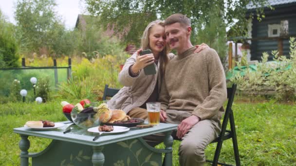 Блондинка і її чоловік беруть селфі на свій смартфон на річницю весілля, вони цілуються в сповільненому темпі — стокове відео