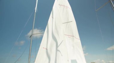 Pahalı bir yatın beyaz yelkeni güneşli bir havada limanda mavi gökyüzüne karşı dalgalanıyor. Yavaş çekim etkisi