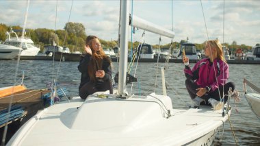 Akıllı telefonları olan genç kızlar pahalı bir spor yatında oturup video blogları için selfie çekiyorlar. Yavaş çekim.