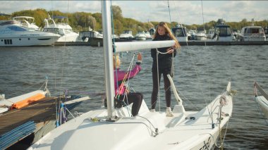 Rıhtımda rüzgarlık giyen iki kız donanımı hızlı beyaz bir yatın patlamasına bağlıyor..