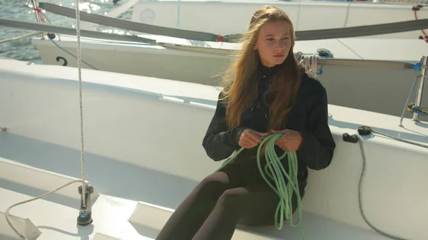 A girl with long hair sitting on the deck of a white sports yacht unwinds a rope to prepare the boat for participation in a multi-day regatta. — Stock Photo, Image