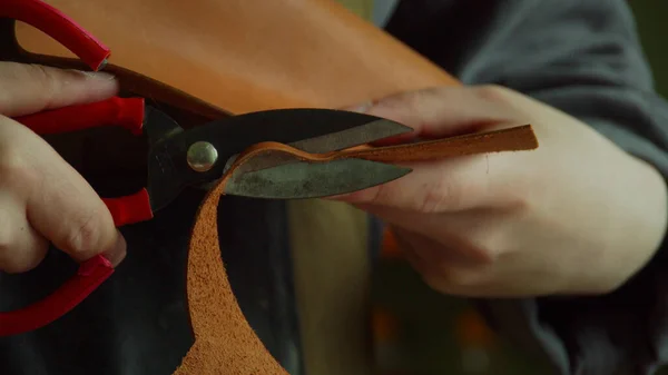 Tanner dans l'atelier découpe un élément en forme de ciseaux tranchants dans un morceau de cuir véritable en gros plan. — Photo