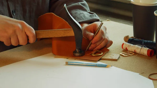 Com um núcleo e um martelo, o curtidor faz furos para costurar um saco exclusivo feito de couro genuíno. Movimento lento. — Fotografia de Stock