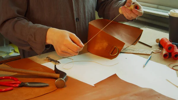 Le maître de la maroquinerie exclusive détache et coupe le fil tailleur avec des ciseaux pour faire un sac en cuir de haute qualité. — Photo