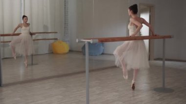 Bale salonundaki güzel dansçı kız ayaklarıyla öne ve yana doğru hareket ediyor, aynanın önünde duruyor.