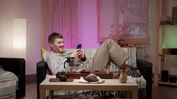 Un hombre en casa en cuarentena chats con un amigo en una red social y hace una ceremonia de té con té chino real. — Foto de Stock