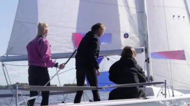 Yavaş çekim yap. Genç bir adam yelkenli teknesinde halat çekiyor nehirdeki yelkenli yarışı sırasında, kızlar yardım ediyor.