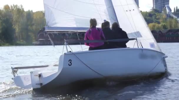 Een jongeman en twee van zijn vrienden varen op een jacht langs de kust, huizen en een skisprong zijn zichtbaar. Langzame beweging. — Stockvideo