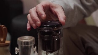Japon çay seremonisi için koyu siyah çay demleyen bir adam cam çaydanlıkta bir zerk makinesiyle..