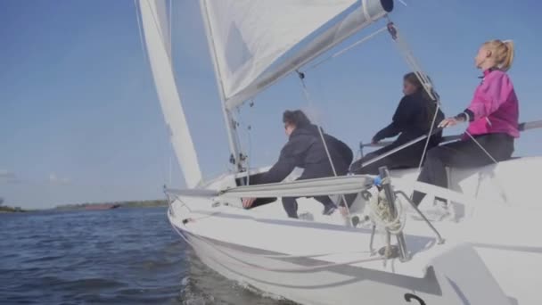 Un jeune homme aux lunettes de soleil et deux charmantes filles contrôlent la voile sur un yacht lors d'un voyage sur la rivière. Effet ralenti. — Video