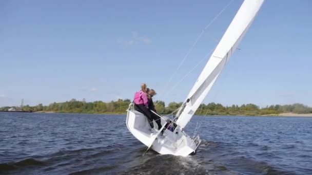 Ein junger Mann und zwei Mädchen schneiden sich in Zeitlupe auf einem weißen Segelboot durch die Wellen des Sees. — Stockvideo