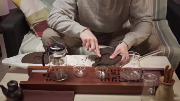 Ceremonia tradicional del té chino oriental en casa. Un hombre recoge piezas de un azulejo de té negro comprimido con un cuchillo de té especial. — Vídeo de stock