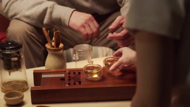 Europejski mąż i żona uczą się prowadzić prawdziwą ceremonię herbaty w domu. Dziewczyna pije herbatę z kubka, facet ją leczy. — Wideo stockowe