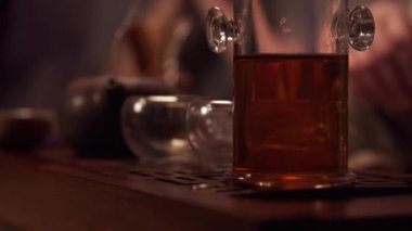 Bir adam kilden demlenmiş bir çaydanlıkta Asya çayı demliyor. Ön planda taze sıcak çayla dolu cam bir kap var..