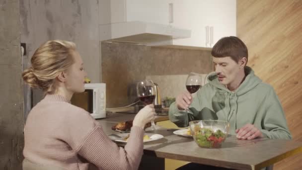 На сімейній вечері молодята п'ють вино, клінкерні окуляри, дружина піклується про чоловіка і кладе салат на тарілку — стокове відео