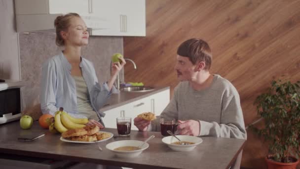 Conversazione a casa in cucina a Colazione di due giovani. Un uomo beve il tè, una ragazza mangia una mela. — Video Stock