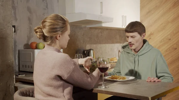 En una cena familiar, los recién casados beben vino, beben copas, la esposa cuida de su marido y pone una ensalada en un plato —  Fotos de Stock