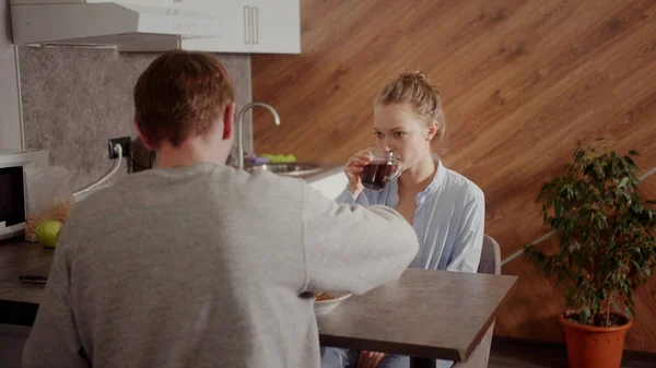 El esposo y la esposa desayunan y toman el té juntos antes del día de trabajo en un acogedor apartamento o casa. La pared está acabada con listones de madera. — Foto de Stock