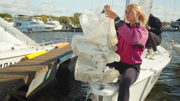 A young athlete in a pink windbreaker ties the staysail to the forestay. Team work of two female sailors. — Stock Photo, Image