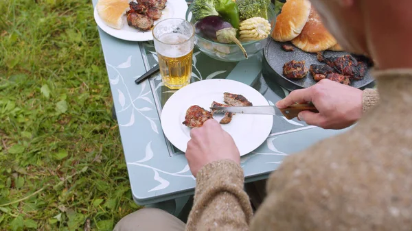 A young couple eats barbecue meat and drinks beer at a table in the courtyard of a country house
