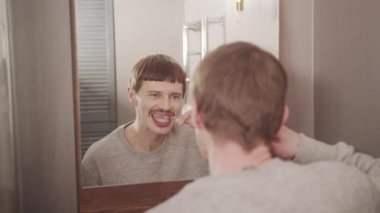 Genç bir adam banyo aynasının önünde dişlerini fırçalıyor, günlük hijyen prosedürü.