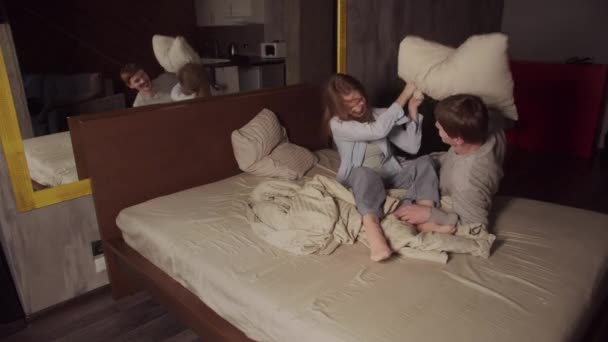 Ein junges Ehepaar vergnügt sich in einem großen Bett in einem Hotel, sie spielen und kämpfen mit Kissen. — Stockvideo