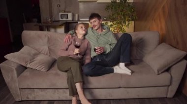 Bir bardak şarapla sıcak bir aile akşamı. Bir erkek ve bir kız kanepede oturup film izliyorlar. Televizyondan stüdyo daireye.