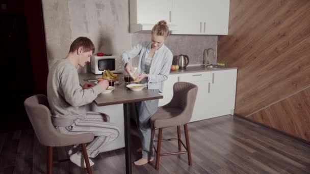 Feliz familia joven, esposa y marido, desayunando en la mesa por la mañana en la cocina sin hijos. Copos de maíz con leche y plátanos. — Vídeos de Stock