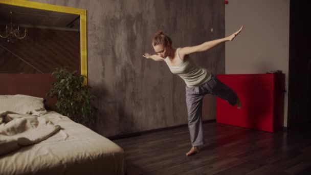 Młoda dziewczyna robi poranne ćwiczenia w domu w pobliżu łóżka w sypialni. Ćwiczenia oddechowe jogi. Flamingo asana — Wideo stockowe