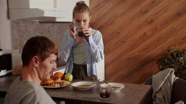 En cámara lenta. Durante el desayuno, el marido observa la hora en el teléfono, la esposa contesta el teléfono y bebe té — Foto de Stock