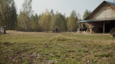 Özel mülk ahırı. Tecrübeli bir binici, üstü kapalı bir ahıra ata biner. Yavaş çekim geniş açı.