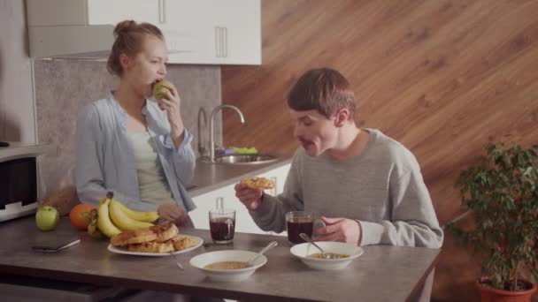 Eine Szene aus dem Familienleben eines jungen Paares. Gemeinsames Frühstück in der neuen Wohnung in der Küche. Frau beißt in einen Apfel. Zeitlupe. — Stockvideo