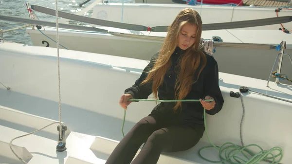 A female athlete checks the rigging while sitting on board a white yacht before traveling down the river on an autumn day — Stock Photo, Image