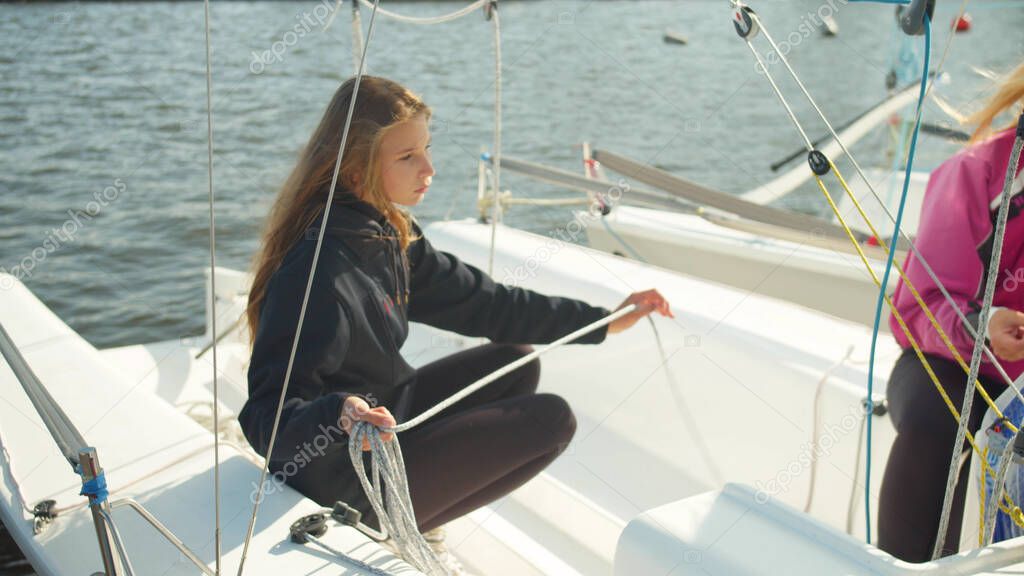 Two cute girls prepare a sailing yacht for departure at the pier on the river with slow motion effect.